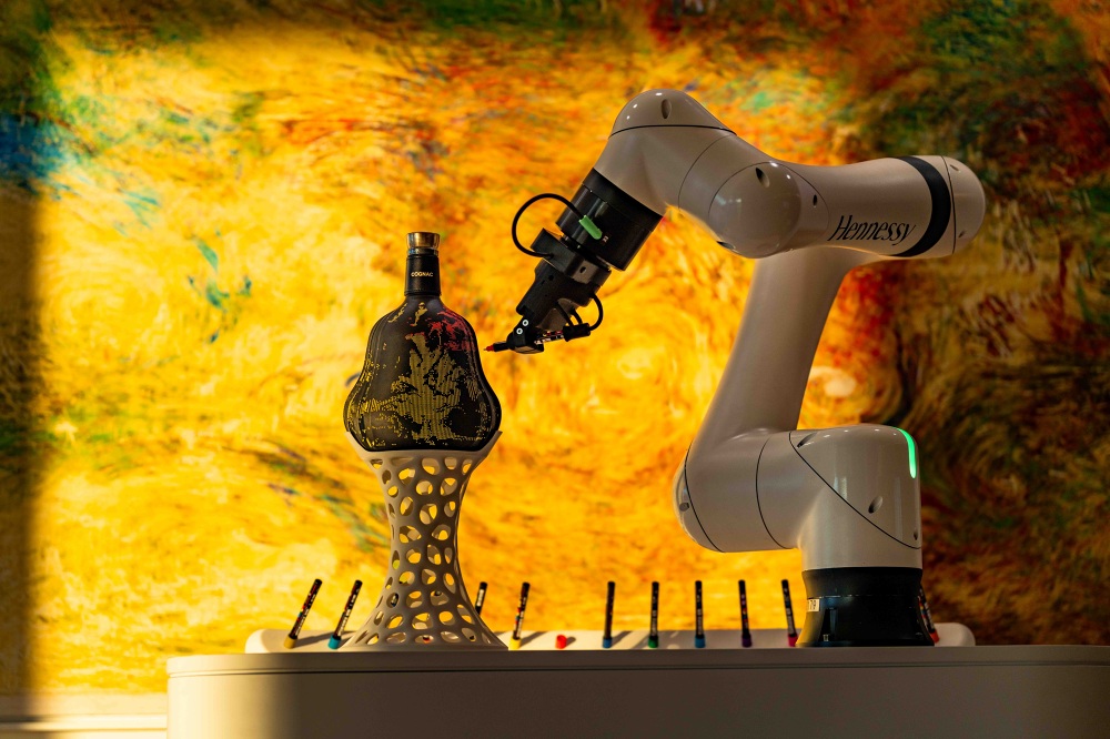 Hennessy-branded robotic arm drawing on a cognac bottle with generative artwork in background